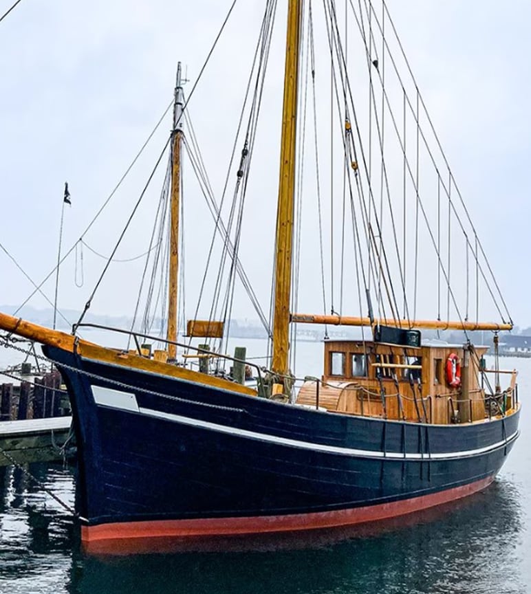 A brown black and red wooden ship parked on the water parked next to a dock.