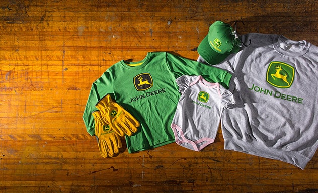 John Deere logo apparel, and hat laid on wooden table.