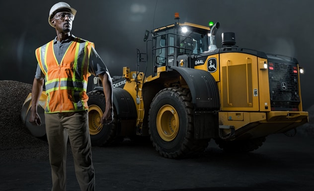 Man in construction gear stands in front of 844L Wheel loader scooping gravel