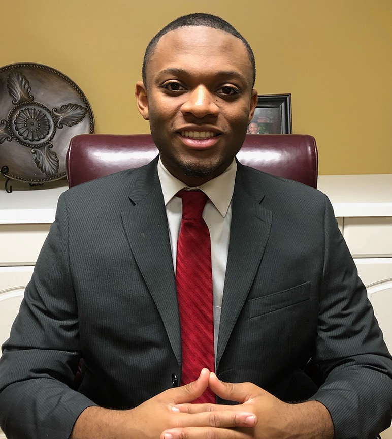 Michael Adams sits smiling at a desk wearing a suit.