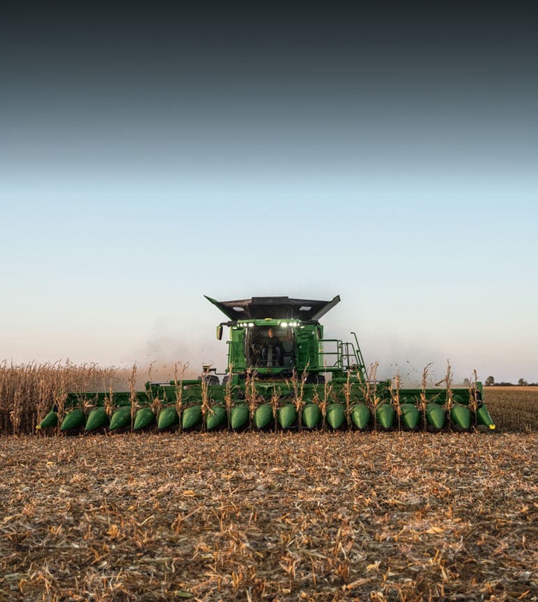 John Deere Harvester harvesting wheat during sunset