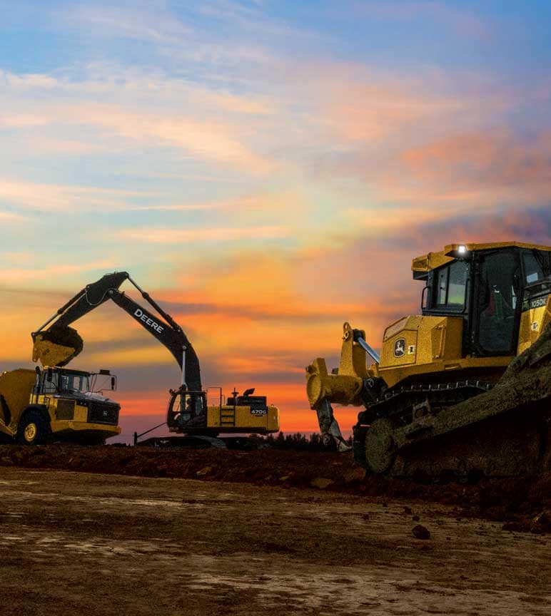 Construction equipment in the field at sunset.