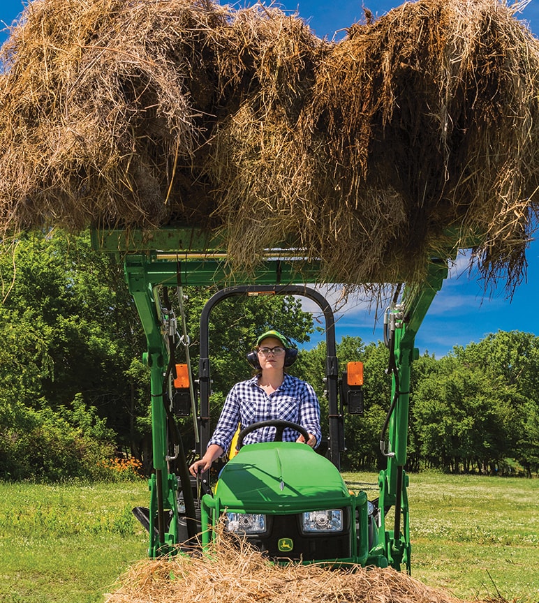 Person using compact tractor to haul hay