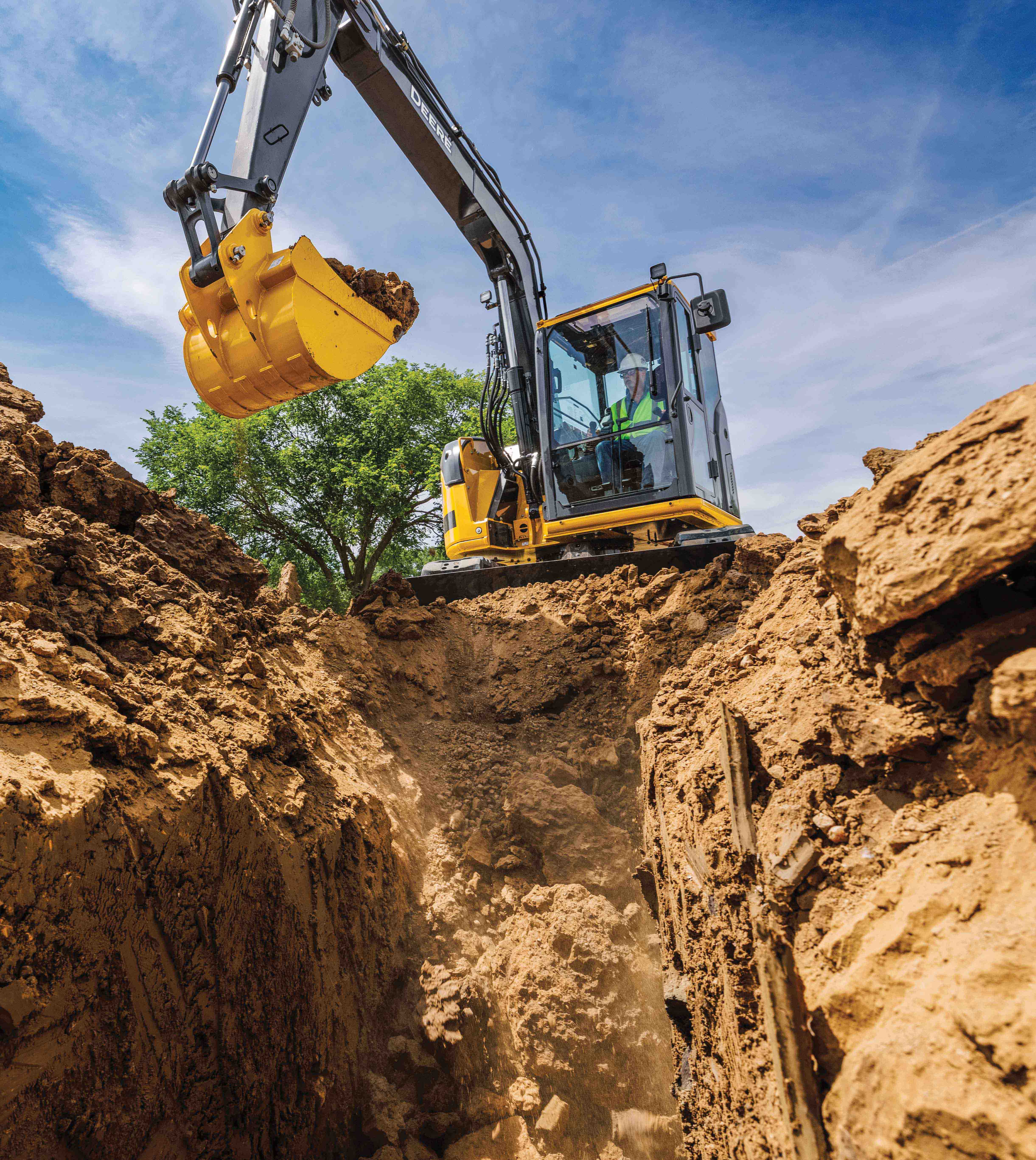 John Deere Excavator works on digging a large hole with blue sky in the background