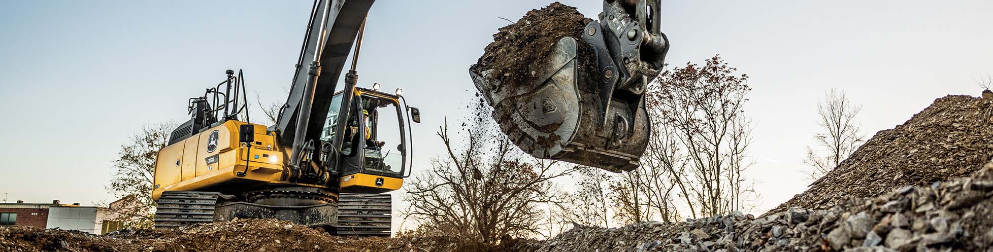 John Deere excavator powerfully lifts a bucket overflowing with dirt