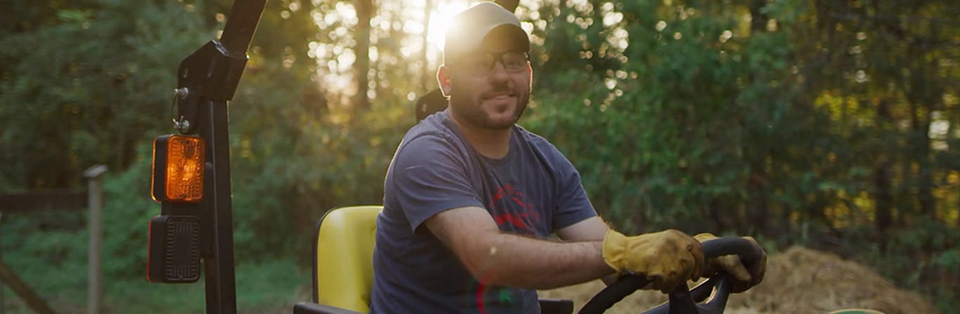 A smiling man on a John Deere lawn mower.