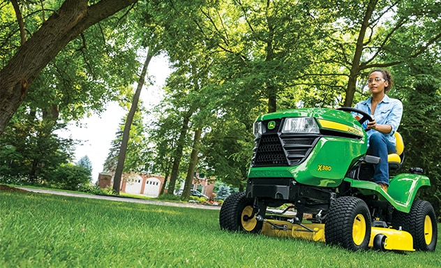 Woman driving John Deere lawn mower outdoors near trees
