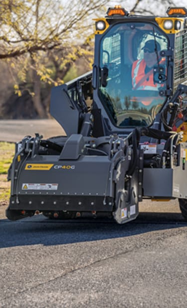 a John&nbsp;Deere 334 P-Tier Skid Steer is using a CP40G cold planer on a street