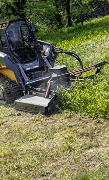 a John&nbsp;Deere 333 P-Tier CTL with an RX 84 Rotary Cutter is cutting tall grass by a treeline