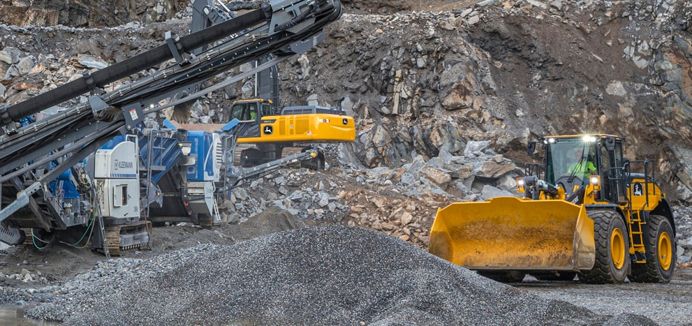 A John Deere excavator and wheel loader along with a Kleeman crusher at work in a rock quarry