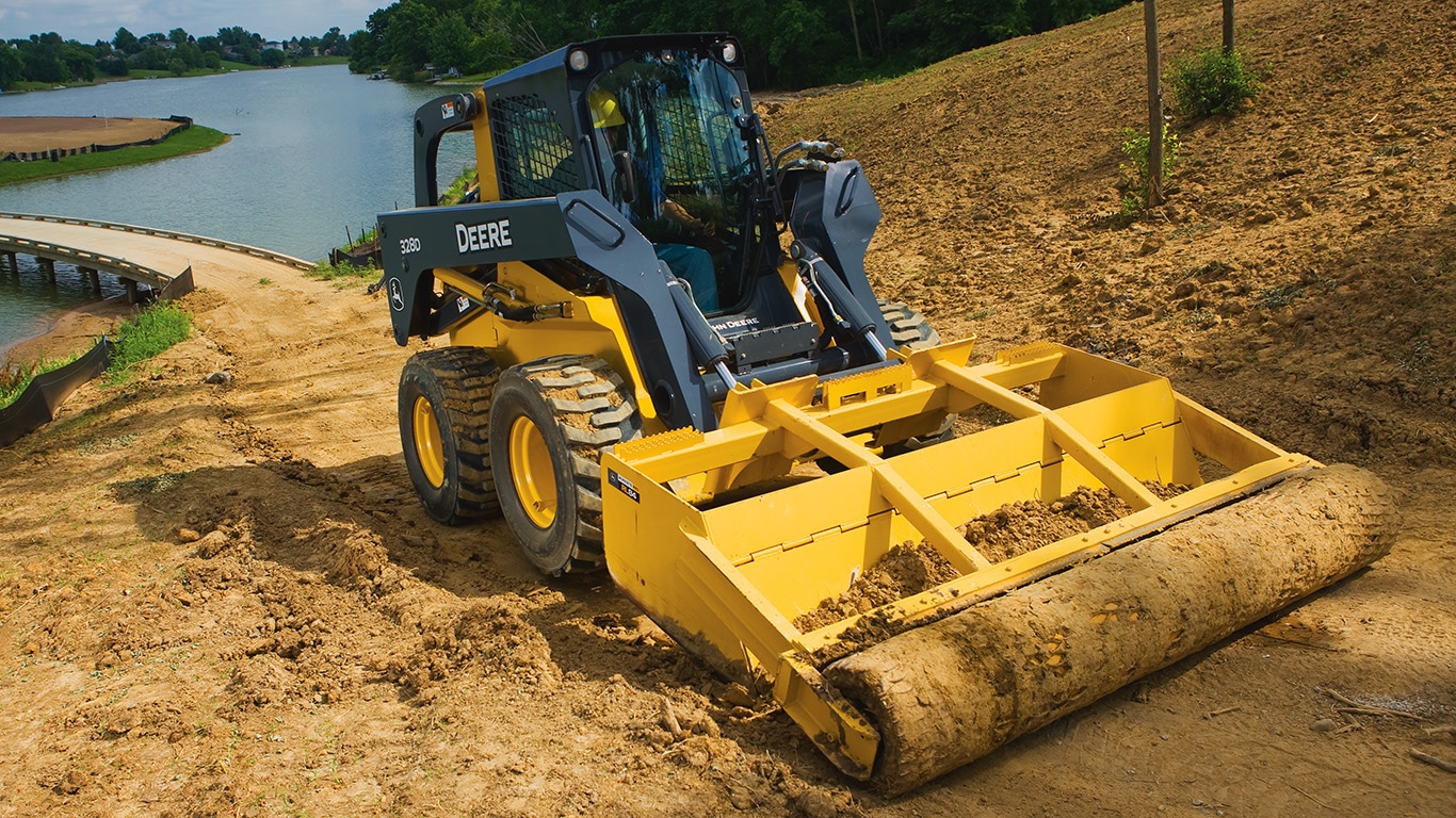 Skid Steer with roller level attachment compacting dirt near a lake.