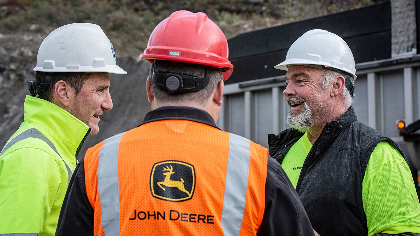 A John Deere dealer talking with two of his customers at a work site.
