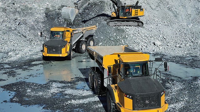 A John Deere large excavator and two ADTs work together at a quarry site.