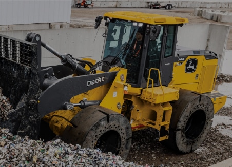 The words â€œwaste handlingâ€ are on top of a John Deere 644 X-Tier Wheel Loader pushing a recycled aluminum pile.