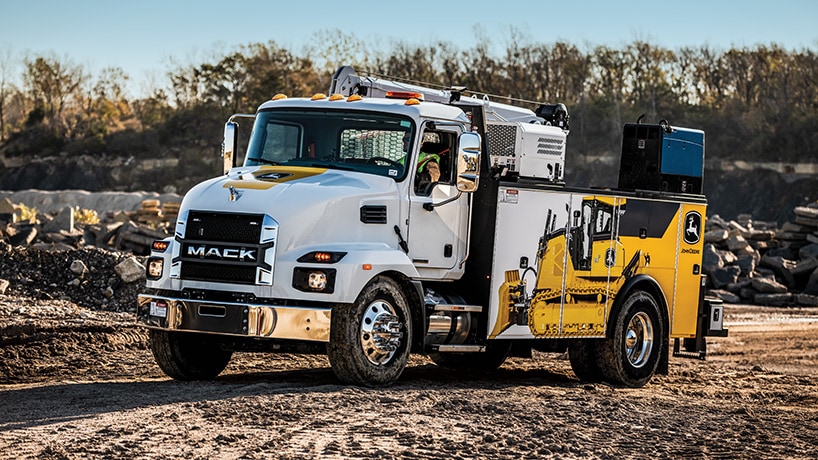 A service truck from a John Deere dealership drives toward the equipment at the jobsite.