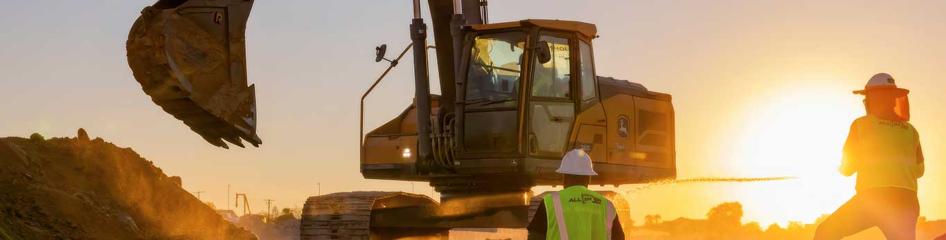 210 P-Tier Excavator works while two people watch with beautiful sunrise in the background.
