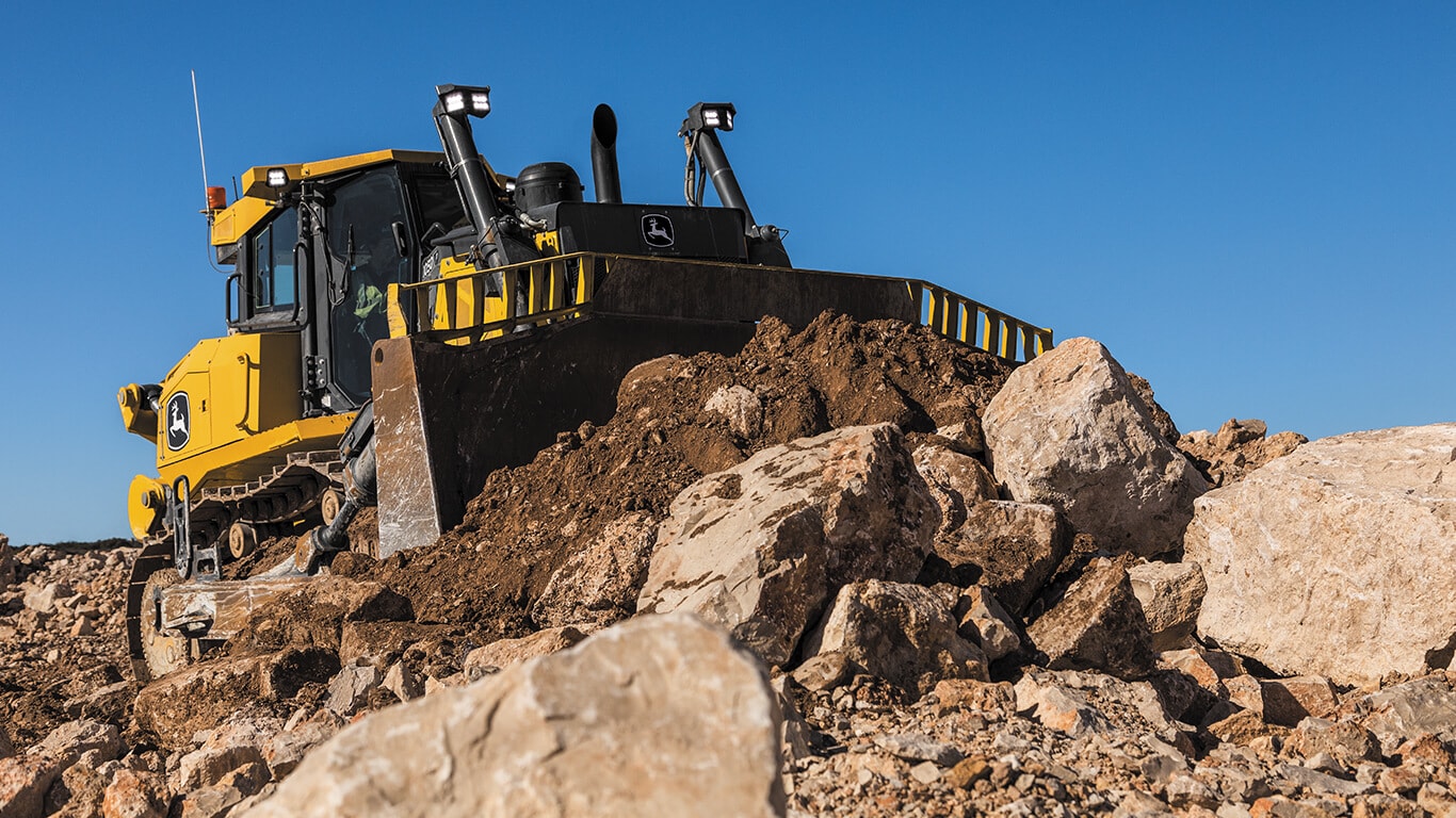 John Deere dozer moving rubble and dirt on job site.
