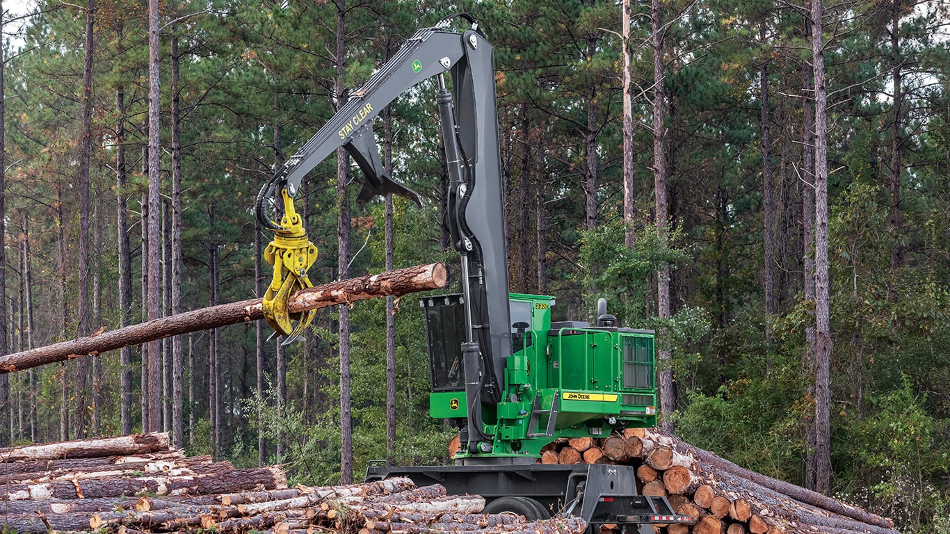 A John&nbsp;Deere knuckleboom loader moving logs in woods