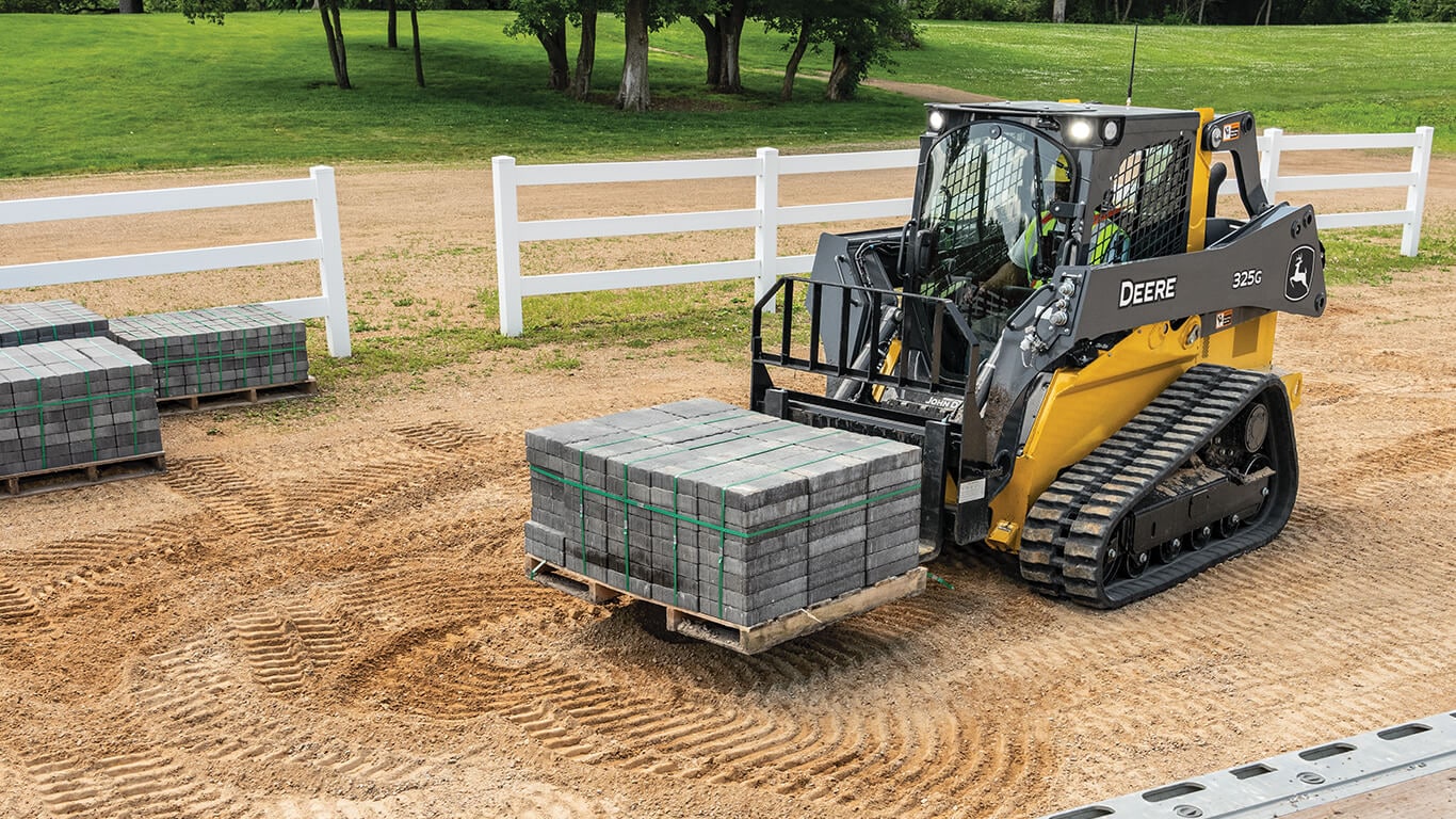 John Deere 325G compact track loader moving pavers on jobsite.