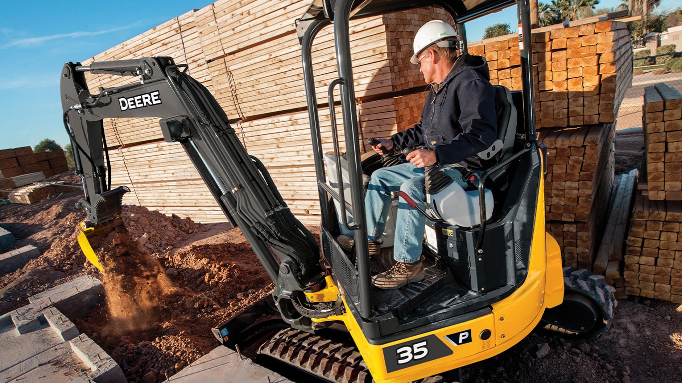John Deere 35 P-Tier compact excavator moving dirt with bucket attachment on job site.