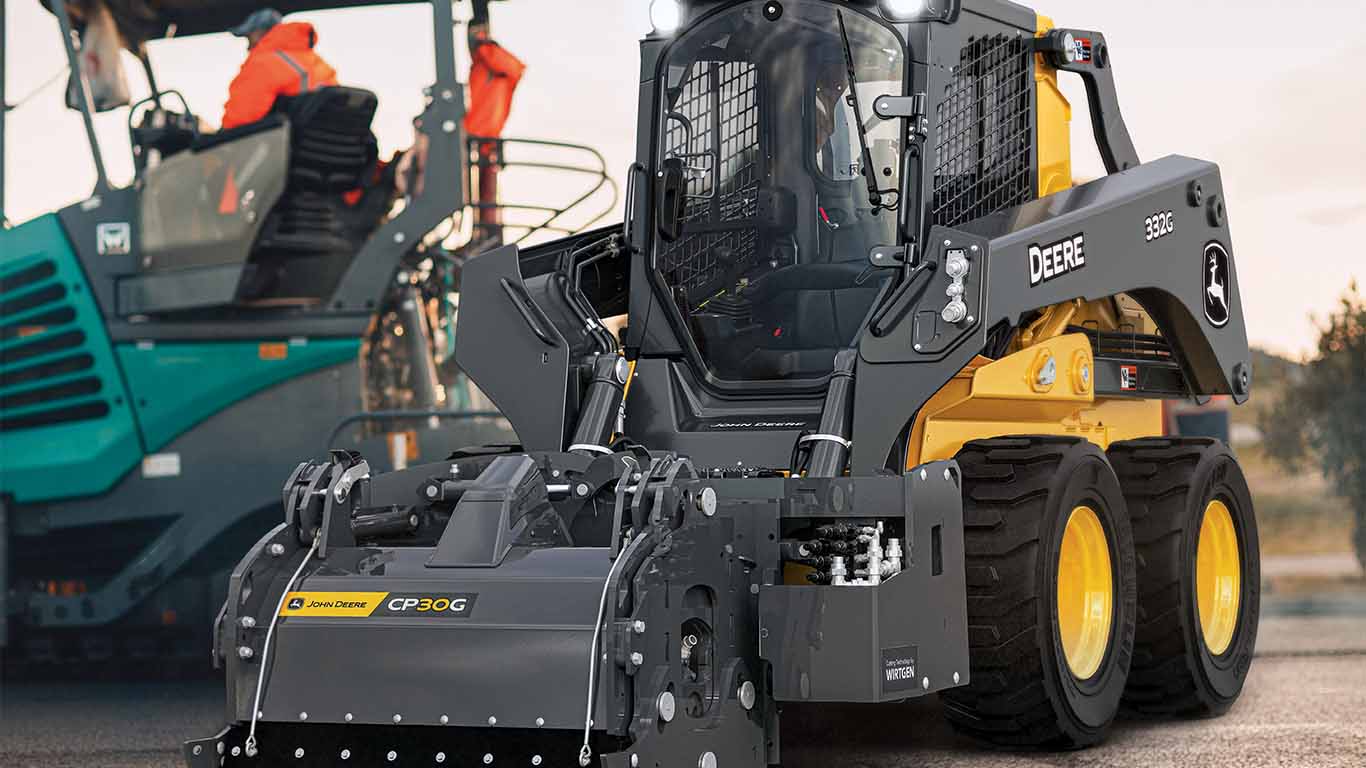 A John Deere 334 P-Tier skid steer with a large cold planer attachment on the front parked on a lot.