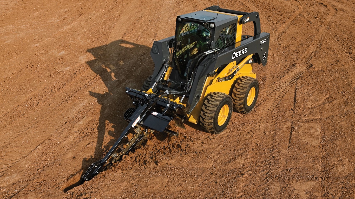 John Deere Skid Steer with a trencher attachment digging a trench through the dirt.