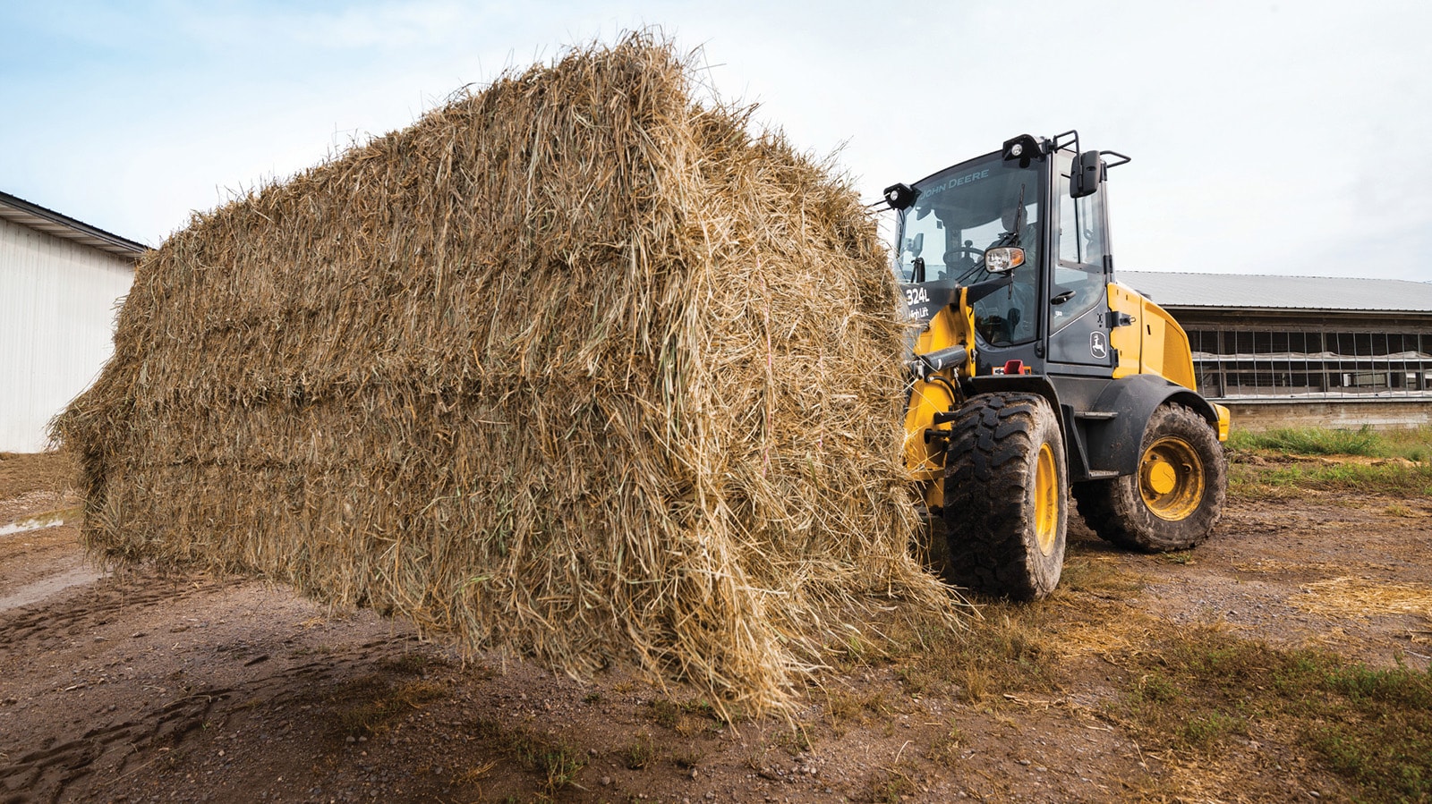 324L High-Lift Compact Wheel Loader hauls a bale of hay through the barnyard.