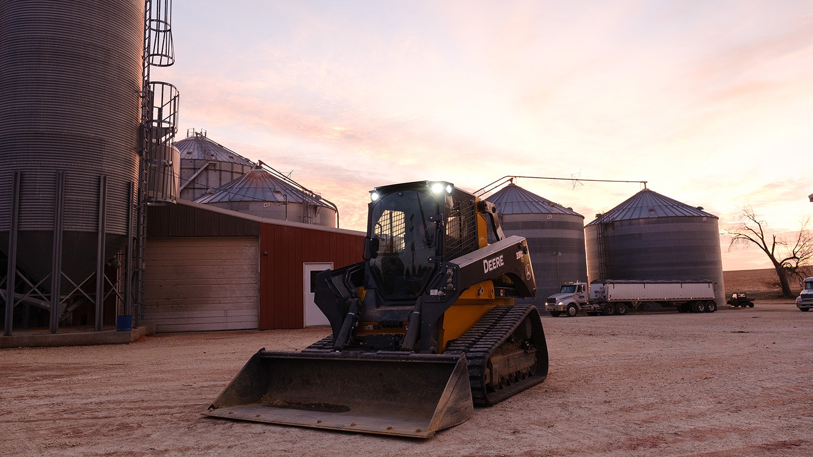 331G Compact Track Loader parked in front of grain bins and storage shed with sunset in the background
