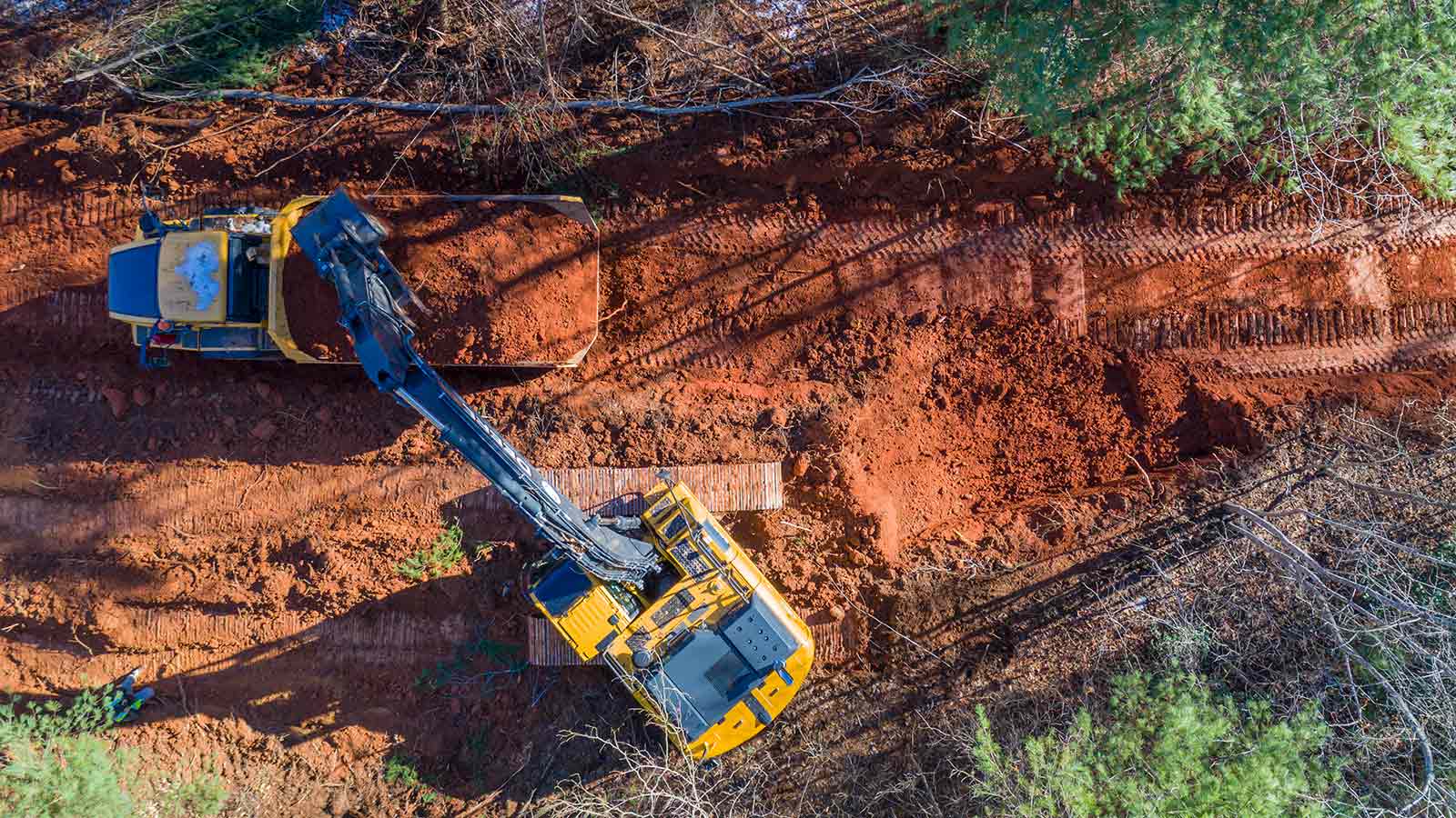 A John Deere 250G Excavator unloads a bucket of dirt into a John Deere 300D Articulated Dump Truck