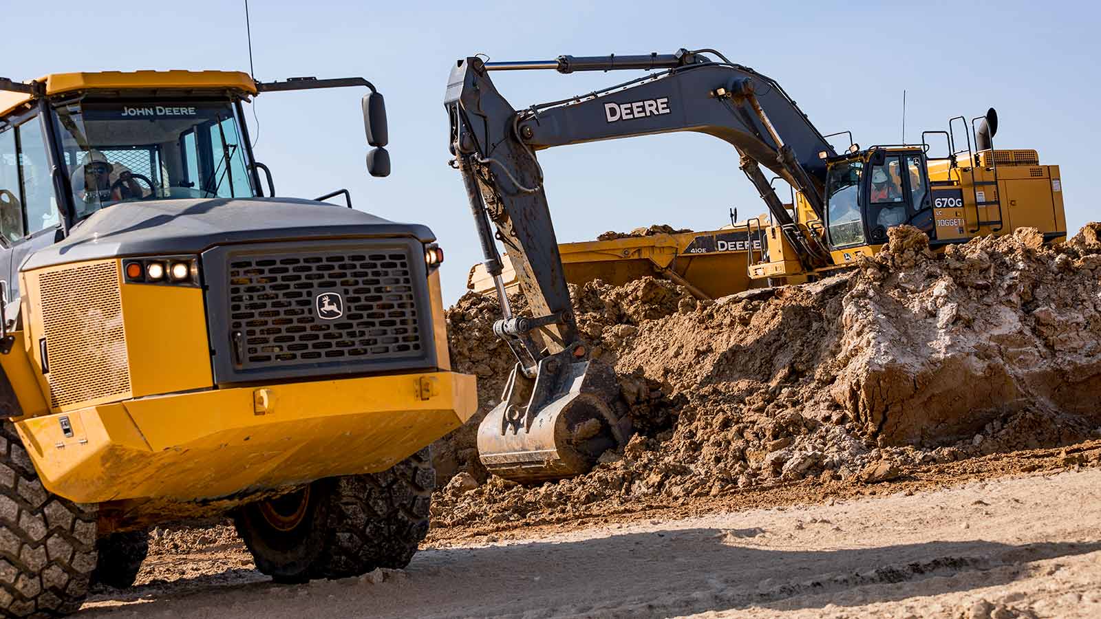 A John Deere 410E ADT is shown with a 670G LC Excavator shoveling dirt in the background.