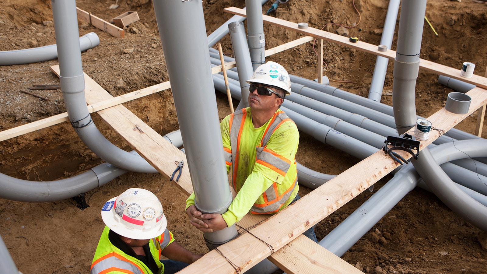 Two men work in a trench, positioning conduit. 