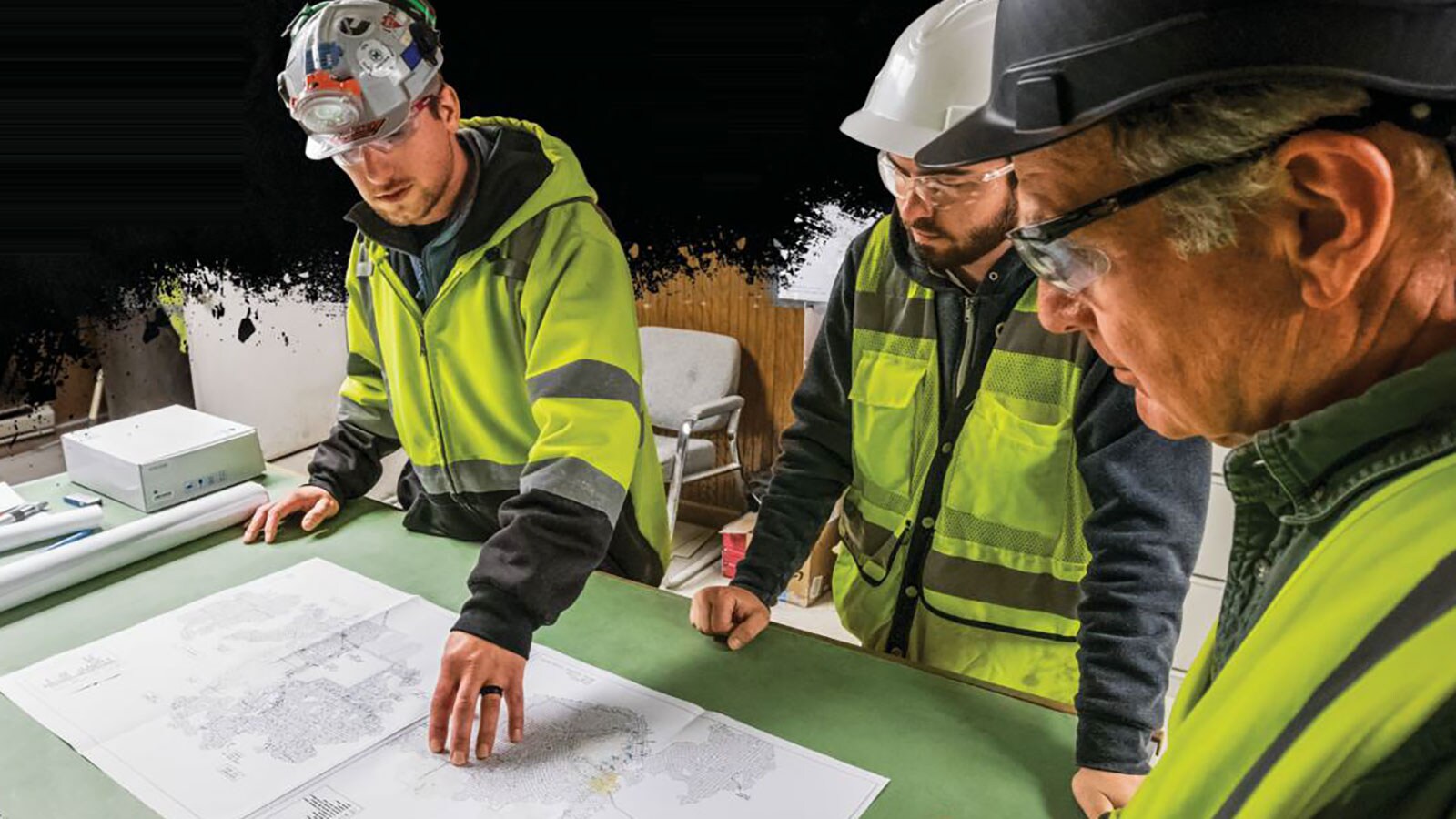 Three miners dressed in hard hat and safety vest review a mining map