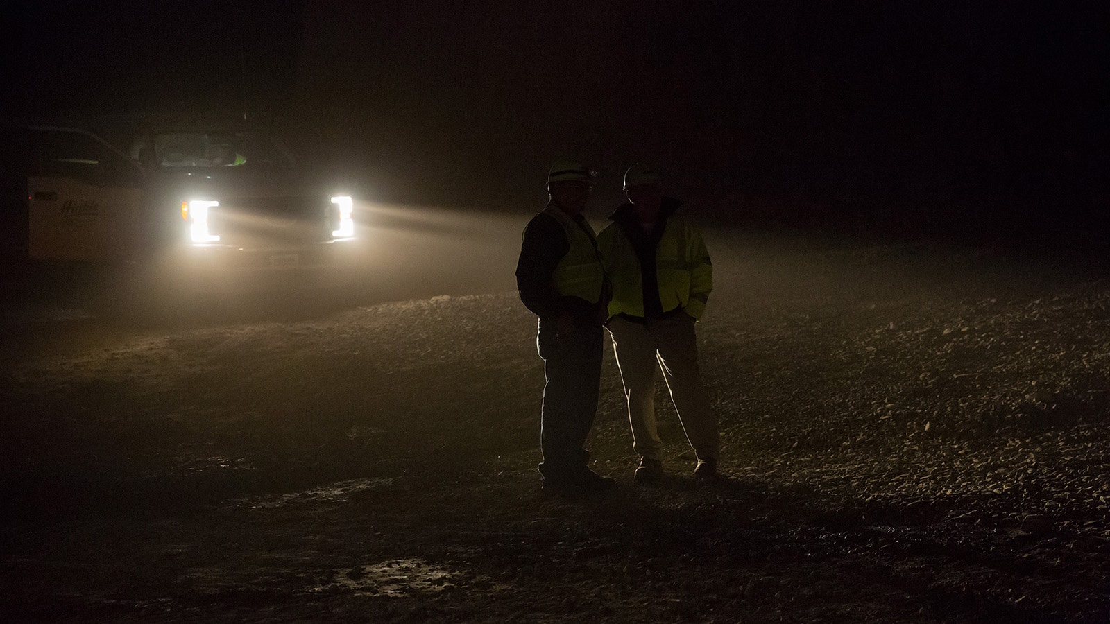 Two workers talk in the headlights of a pickup truck in the mine
