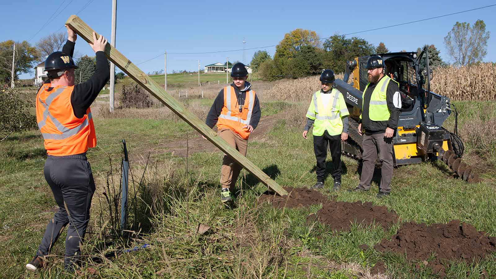Students erecting posts with the help of a compact track loader and auger.
