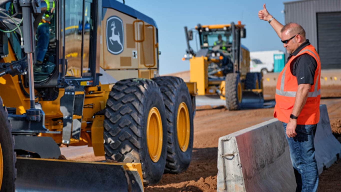 Man giving thumbs up to driver of a motor grader