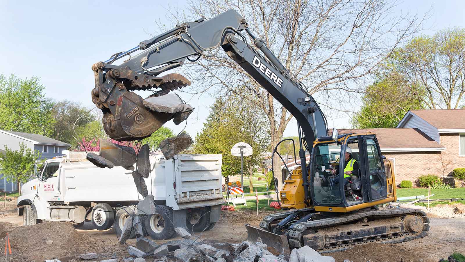 A John Deere excavator tears up a residential street