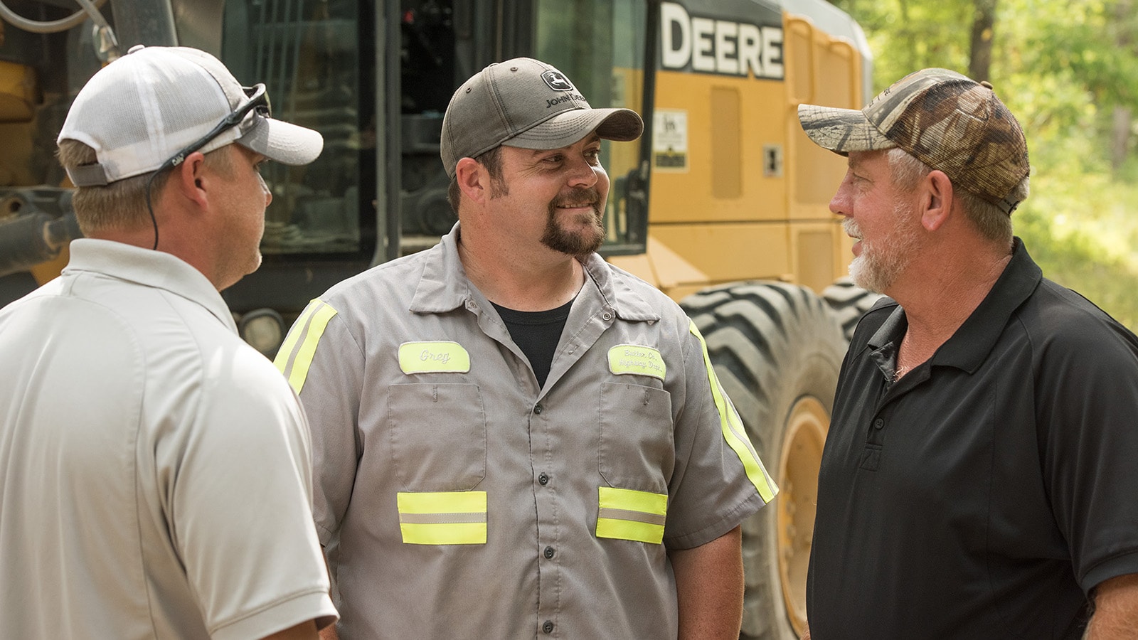 close up of two men talking with their John Deere dealer representative in front a 770g motor grader