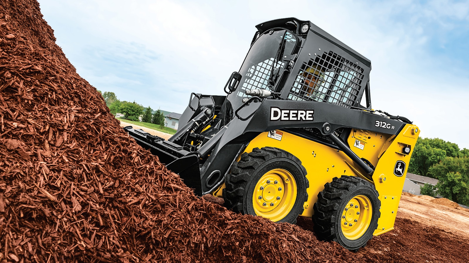 312GR Skid Steer scoops up a bucket of red mulch from a large pile