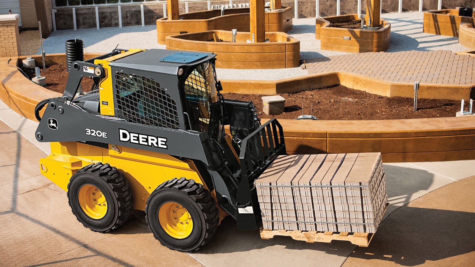320E Skid Steer with pallet fork attachment carries a load of paving stones