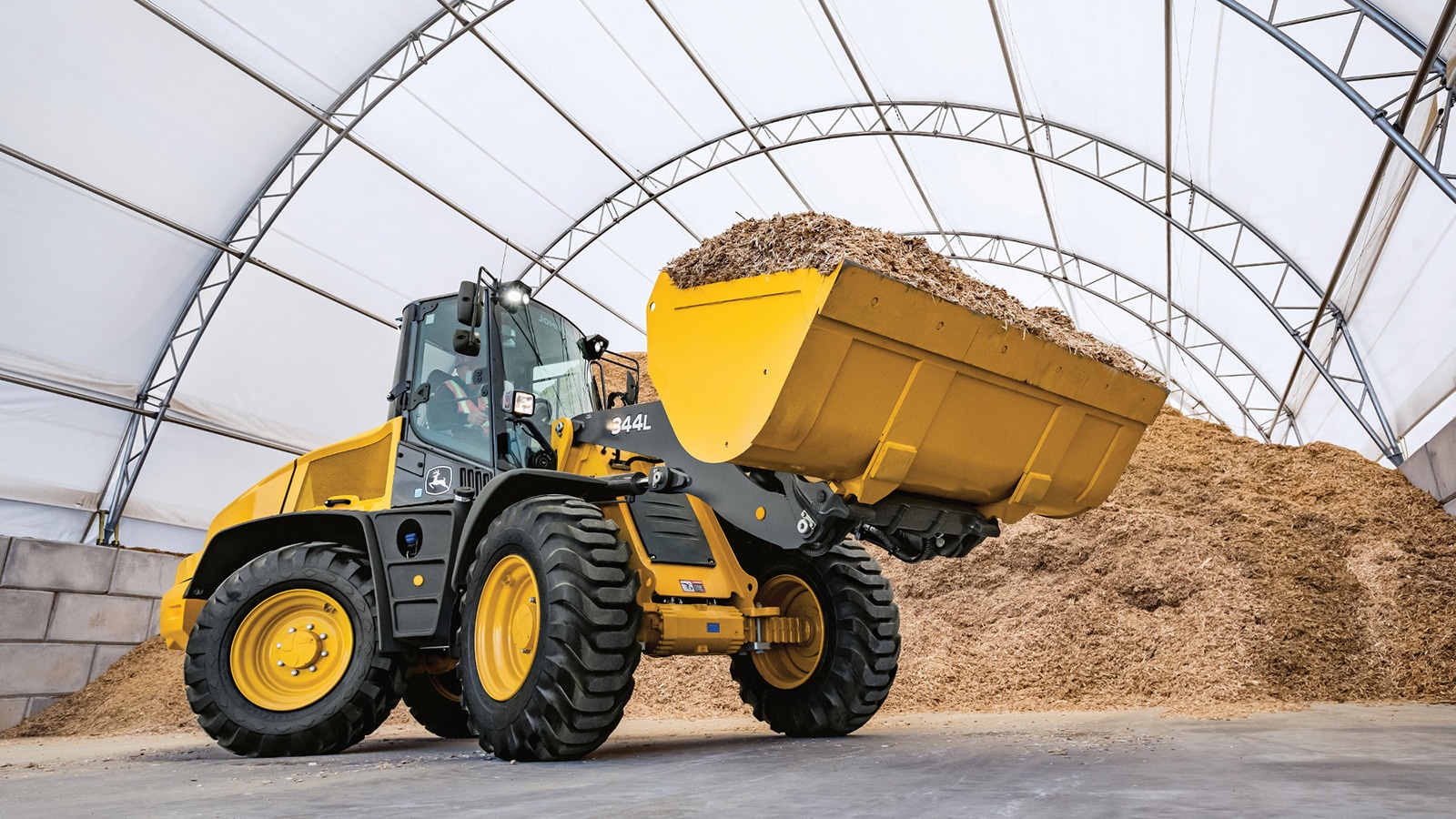 344L loader carries a bucket full of mulch inside a hoop building
