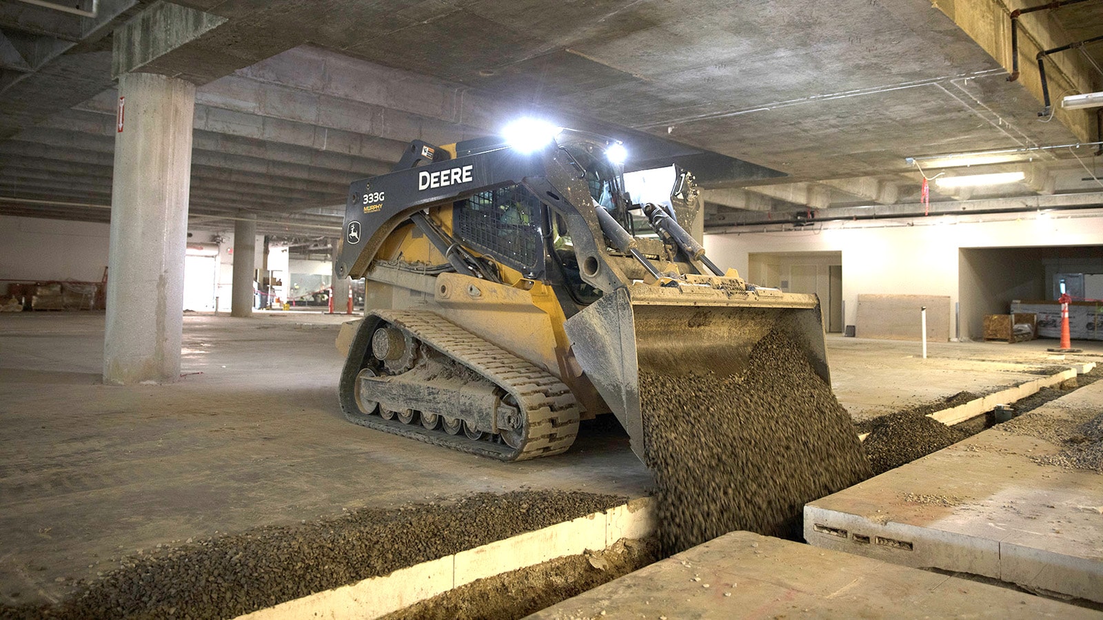 333G Compact Track Loader dumps a load of dirt into a gap in a parking garage site