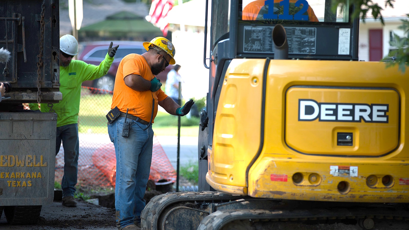 Workers direct a compact excavator operator on a residential jobsite