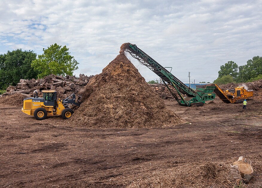 a conveyor drops mulch into a pile, while a wheel loader scoops loads off of the pile