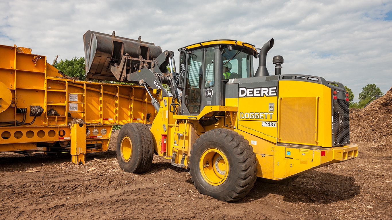 A 624K wheel loader dumps wood scraps into a grinder machine