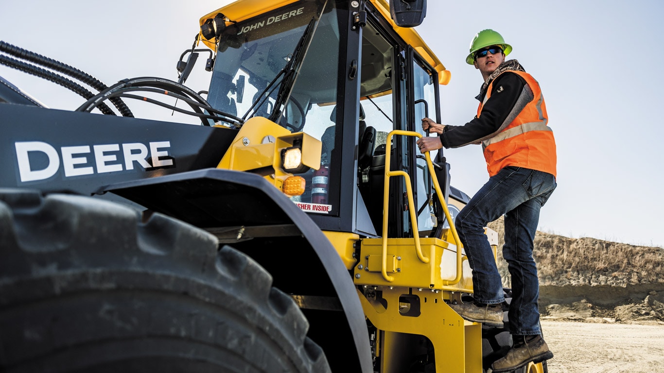 Worker climbing to a John Deere wheel loader on job site.