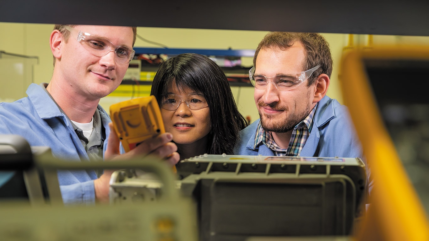 Three people working together on an electronic component
