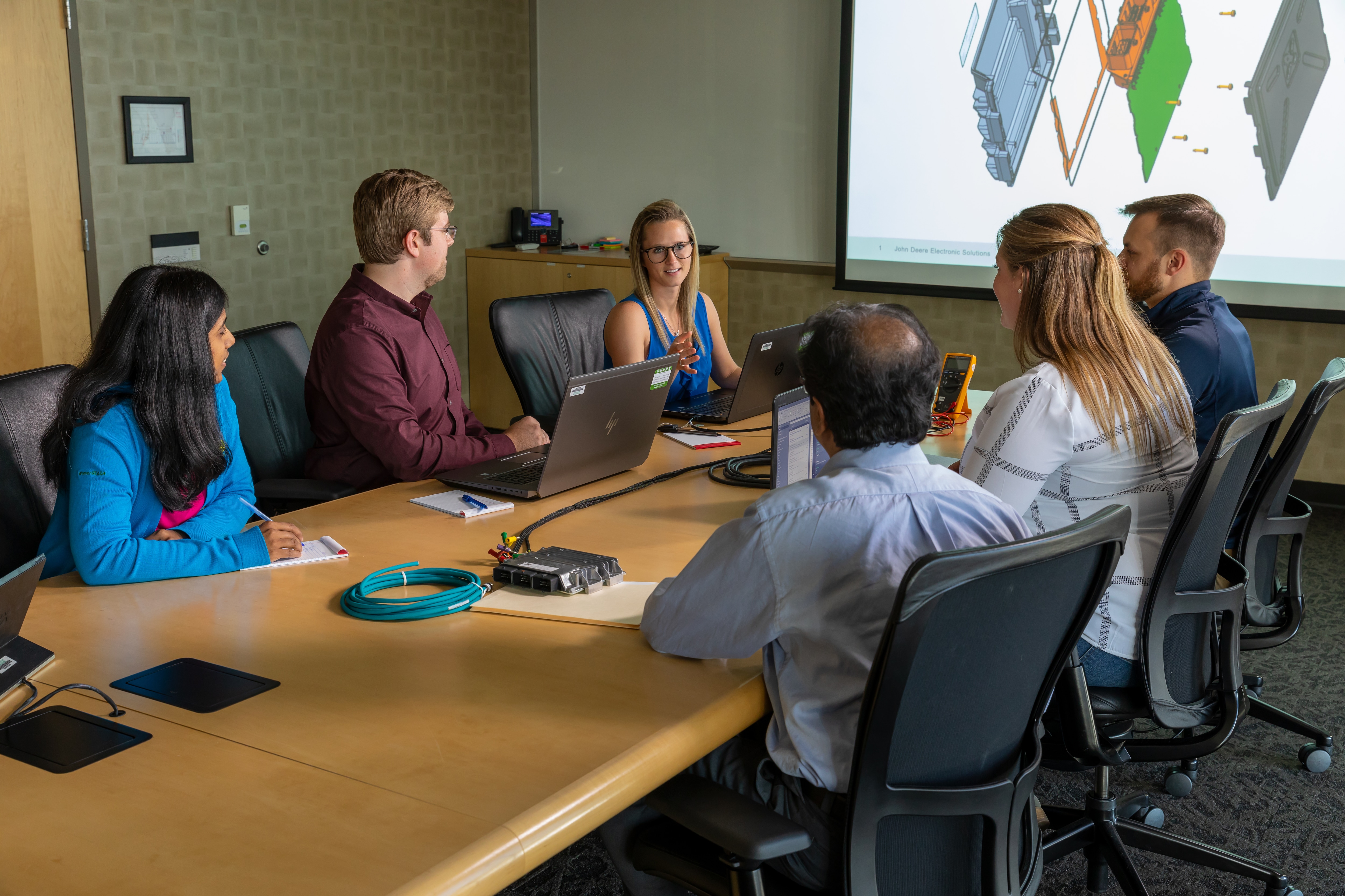 the John&nbsp;Deere Electronics Program Management team working around a conference table with laptops and a projector presentation.