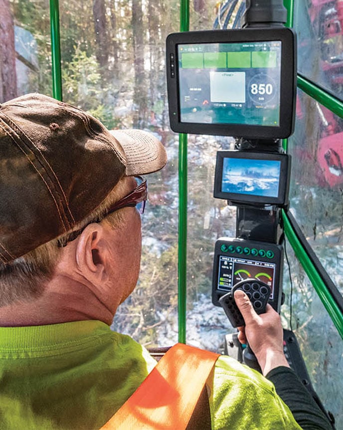 Man running forestry equipment looking at multiple displays in cab