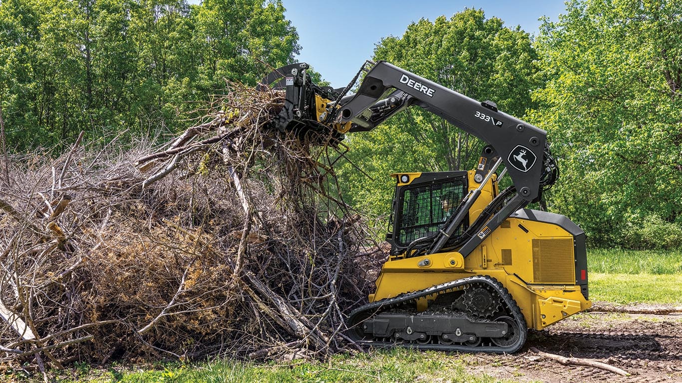 333 P-Tier compact track loader using a grapple attachment to clear a pile of branches.