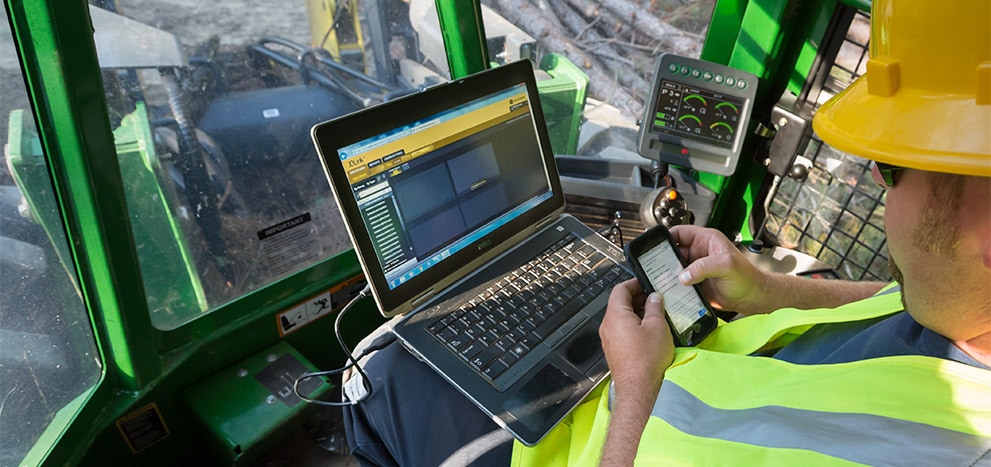 Logger in cab using laptop and smartphone for machine monitoring and diagnostics.